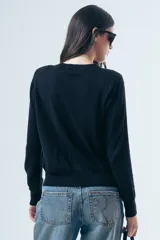 Cardigan negro de punto fino, con cuello redondo, cierre frontal de botones y mangas largas con puños ajustados.