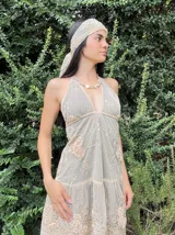 Vestido corto negro con escote en V profundo, estilo halter con tiras para atar al cuello. Presenta un diseño ajustado en el busto con tiras ajustables bajo el mismo que se cruzan y anudan en la espalda, y falda con volado en el ruedo con detalle de encaje.