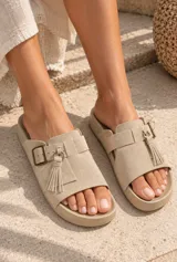 Sandalias de gamuza color tostado, de diseño abierto con tira ancha en el empeine decorada con una hebilla metálica y flecos colgantes.