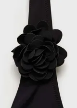 Traje de baño enterizo negro con escote halter y detalle de flor aplicada en el frente. Presenta espalda descubierta y cierre de lazo en el cuello.