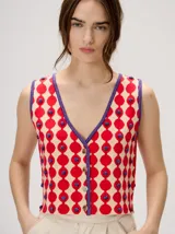 Top de punto sin mangas con escote en V, cierre frontal con botones y estampa geométrica de círculos rojos sobre fondo beige, con detalles en color violeta y apliques en relieve.