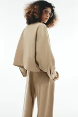 Cazadora bomber de color beige con cuello subido, manga larga y bolsillos delanteros. Cuenta con cierre frontal de cremallera metálica y cordón ajustable en el dobladillo.