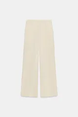 Pantalón gris de tiro alto con bolsillos delanteros y traseros, detalle de pliegues frontales y cierre frontal con cremallera y botón.