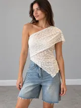 Top de encaje blanco con diseño asimétrico de un solo hombro y dobladillo en punta.