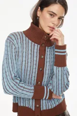 Cardigan de punto con diseño de ochos, color celeste con detalles en marrón. Cuenta con cuello alto, cierre frontal de botones y puños y ruedo acanalados.