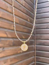 Collar de cristales facetados en tono marrón con pequeñas cuentas doradas, con dije circular con baño en oro, fondo de nácar y una cruz en relieve rodeada de circonias.