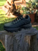 Championes de trekking color negro con suela de goma dentada para mayor tracción. Presenta cordones moteados con detalles en amarillo y refuerzos laterales.