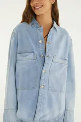 Camisa de jean de corte amplio con cuello camisero, cierre frontal con botones metálicos y grandes bolsillos frontales con solapa.