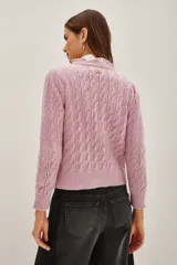 Cardigan de punto calado en color rosado, con cuello redondo y cierre frontal de botones decorativos con pedrería brillante.