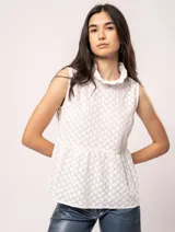 Blusa blanca sin mangas, con cuello alto con volados y detalles bordados con motivos florales.