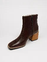 Botin de cuero y gamuza color marrón, con diseño combinado de paneles lisos y gamuzados, puntera cuadrada y taco bloque de madera con diseño geométrico. Cuenta con cierre lateral interno.