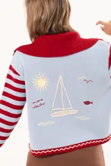 Saco tejido de punto a rayas horizontales en color celeste y rojo, con cuello alto, cierre frontal doble deslizador y puños con diseño en contraste. Presenta un pequeño bordado en el pecho.