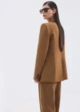 Blazer cruzado de lino y viscosa color marrón tostado, de corte recto y largo, con cuello pico con solapa de muesca, bolsillos laterales con solapa y cierre de doble botonadura.