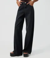 Pantalón wide leg de denim negro, con cintura media, bolsillos funcionales, presillas para cinturón y cierre frontal con botón y cremallera.