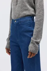 Jean de denim azul de tiro alto, con corte recto holgado, pliegues frontales y cierre con botón y cremallera.