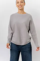 Buzo tejido de punto en color beige, con cuello redondo, mangas largas y silueta relajada con dobladillo irregular, siendo más largo en la parte trasera.
