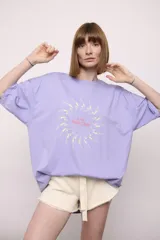Remera lila de corte holgado con mangas cortas y estampado circular con figuras de nadadoras y texto "The Ped Swim Club".