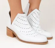 Botín de cuero blanco con textura de crocco y charol, diseño con calados circulares y aberturas laterales en forma de V. Cuenta con taco foliado de madera y vira cosida.