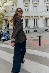 Camisa de cuello solapa y manga larga, color marrón con rayas verticales blancas. Presenta cierre frontal con botones ocultos y dos hebillas decorativas en color beige en el lateral.