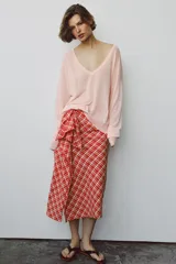 Falda midi de tiro medio ZARA WOMAN COLLECTION confeccionada en hilatura con algodón, con estampado de cuadros en tonos rojos y blancos. Presenta detalle de pliegue con lazadas en el delantero y bajo recto con abertura. Cierre con cremallera oculta en costura.