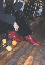 Bota corta tipo texana en cuero acharolado color bordó, con punta afinada, taco bajo y costuras decorativas en el empeine.