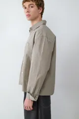 Camisa de mangas largas color beige con estampado a cuadros pequeños, corte boxy y cierre frontal con botones. Presenta cuello con solapa y un bolsillo de parche en el pecho.