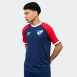 Remera de algodón azul con mangas raglán rojas y detalles en blanco en cuello y puños. Incluye logo de Umbro bordado en el pecho y escudo del Club Nacional de Football.
