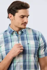 Camisa de manga corta con estampado de cuadros en tonos celestes, azules, blancos y verdes, con cierre frontal de botones y bolsillo ojal en el pecho.