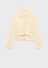 Cardigan de punto color crema con cuello camisero, cierre frontal con cremallera y cinturón ajustable con hebilla en la cintura. Presenta un diseño recto de manga larga.