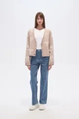 Cárdigan color beige con estampado de moños blancos, escote en V y cierre frontal con botones.