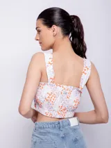 Top blanco con estampado floral en tonos naranja y lila, de corte cropped y breteles anchos.