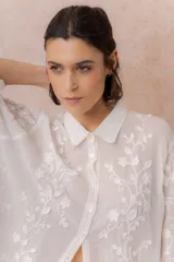 Camisa blanca de calce relajado con tejido semitransparente y bordados florales en relieve. Cuenta con cuello camisero, abotonadura frontal y mangas amplias.
