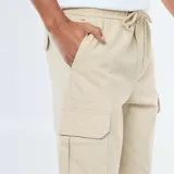 Pantalón cargo color beige, de corte estándar, con múltiples bolsillos laterales y cintura elástica con cordón ajustable.