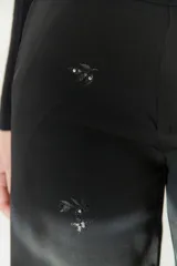 Pantalón negro de corte amplio con cintura alta, cierre de cremallera y botón. Cuenta con bolsillos laterales y tela bordada.