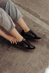 Zapatillas negras con paneles laterales de efecto piel de serpiente metalizado en tonos bronce y negro. Tienen cordones negros y suela de goma color caramelo.