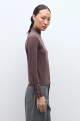 Media polera de manga larga con cuello alto y detalle de frunces en los puños, confeccionada en tejido suave y elástico.