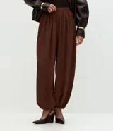 Pantalón de corte balloon con cintura alta elástica y diseño amplio. Presenta una caída fluida con terminaciones ajustadas en los tobillos que generan un efecto abullonado.