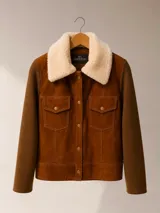 Campera de estilo trucker con cuerpo de gamuza marrón y mangas de tejido de punto. Presenta cuello de corderito sintético en color crema, cierre frontal con botones metálicos y dos bolsillos delanteros con solapa.