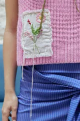 Chaleco tejido color verde oliva con sisas amplias y largo cropped. Posee detalle de parche bordado a mano con flores y detalles en hilo.