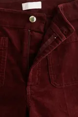 Pantalón de pana color bordó, de tiro alto, con bolsillos de parche delanteros y traseros. Presenta cierre con botón y piernas acampanadas con pliegues.