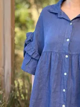 Vestido camisero blanco de lino italiano, con cuello camisero, cierre frontal con botones, mangas cortas con doble volado y bolsillos laterales.