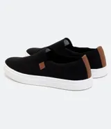 Championes tipo slip on marca Viko, de color negro con suela de goma blanca. Presenta un diseño minimalista sin cordones con paneles elásticos laterales y un pequeño detalle de etiqueta en color marrón.