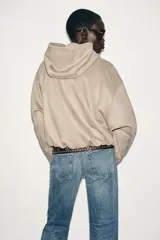 Chaqueta bomber de efecto ante en color marrón, con capucha ajustable mediante cordones, cierre frontal con cremallera, bolsillos laterales y bajo con elástico interior.
