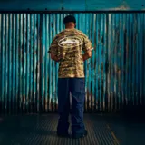 Remera de manga corta con estampado de camuflaje digital en tonos verdes y marrones. Presenta un gráfico central en color blanco dentro de un óvalo que representa una isla.