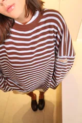 Sweater oversize de punto con diseño a rayas horizontales en color verde y blanco, cuello redondo en contraste rojo y detalle de etiqueta bordada en la manga.