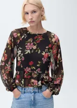 Blusa negra semitransparente con estampado floral en tonos rojos y rosas, volantes en el bajo, cuello redondo, manga larga abullonada y cierre de lazo en el cuello.