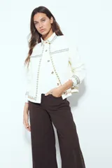 Campera de jean color blanco con bordados geométricos en cuello, delantero, bolsillos, puños y ruedo. Tiene botones dorados y un calce recto y relajado.