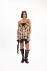 Vestido corto sin mangas con tirantes finos, diseño en capas con superposición drapeada de tela a cuadros tipo tartán en tonos beige y marrón sobre una base de tela marrón lisa.