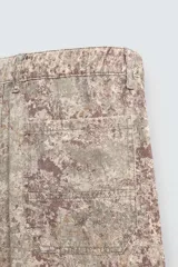 Pantalón de corte relajado confeccionado en tejido ligero de algodón con estampado abstracto de efecto lavado. Presenta cintura elástica, bolsillos frontales y bolsillos traseros de plastrón, con cierre frontal de cremallera y botón.