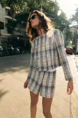 Falda pantalón de tiro alto confeccionada en tejido de tweed con estampado a cuadros en tonos beige, azul y negro. Presenta detalles de falsos botones y cierre lateral con cremallera oculta.